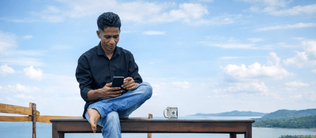 Abdullah Burhan (Kopa), Ketua IKRAR Batam, duduk di bangku dengan latar pemandangan perairan dan perbukitan.